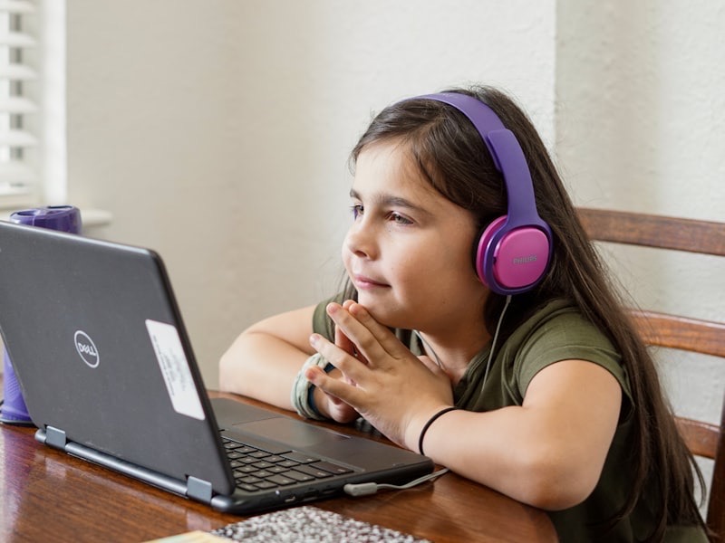 A young child wearing headphones and smiling at a laptop during an online session