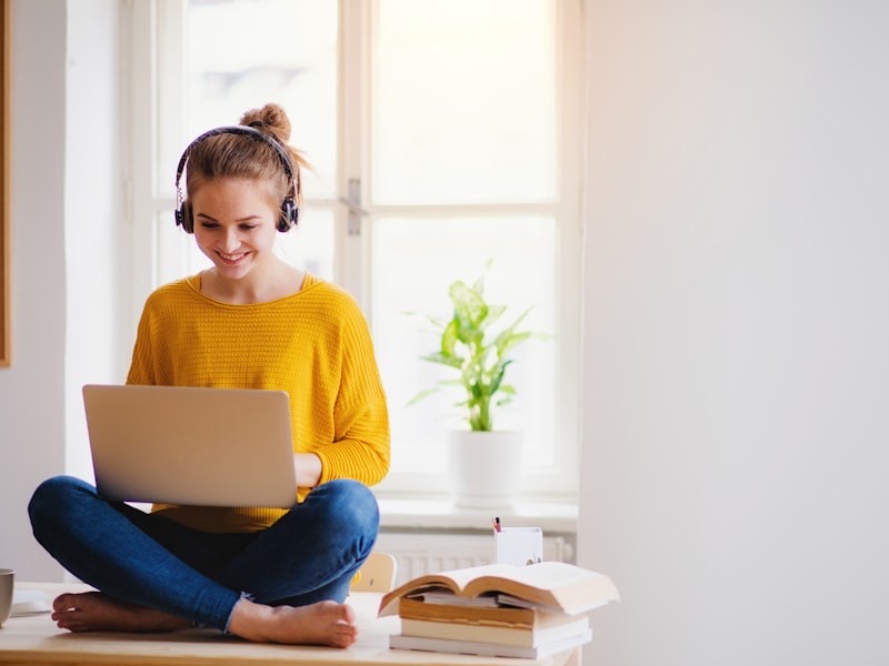 An adolescent in a green hoodie focused on a laptop at a desk