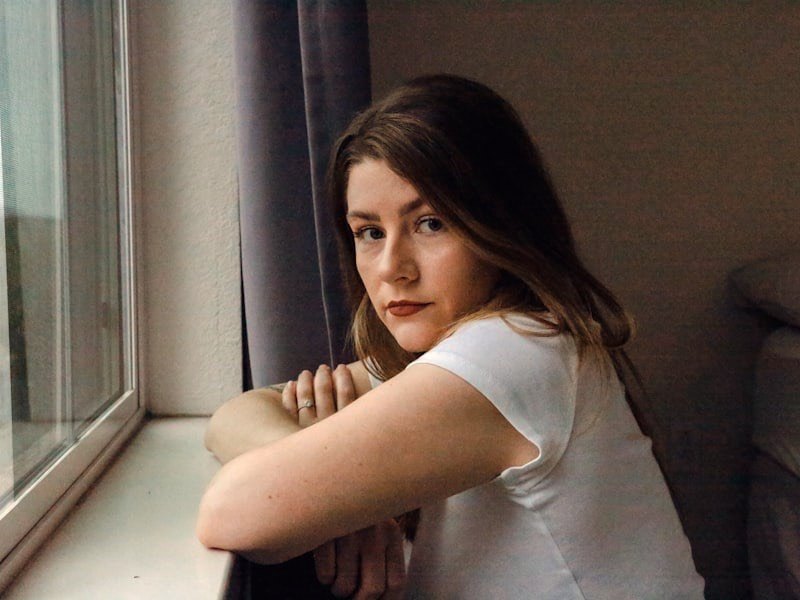 A thoughtful adolescent sitting near a bright window in soft, warm light